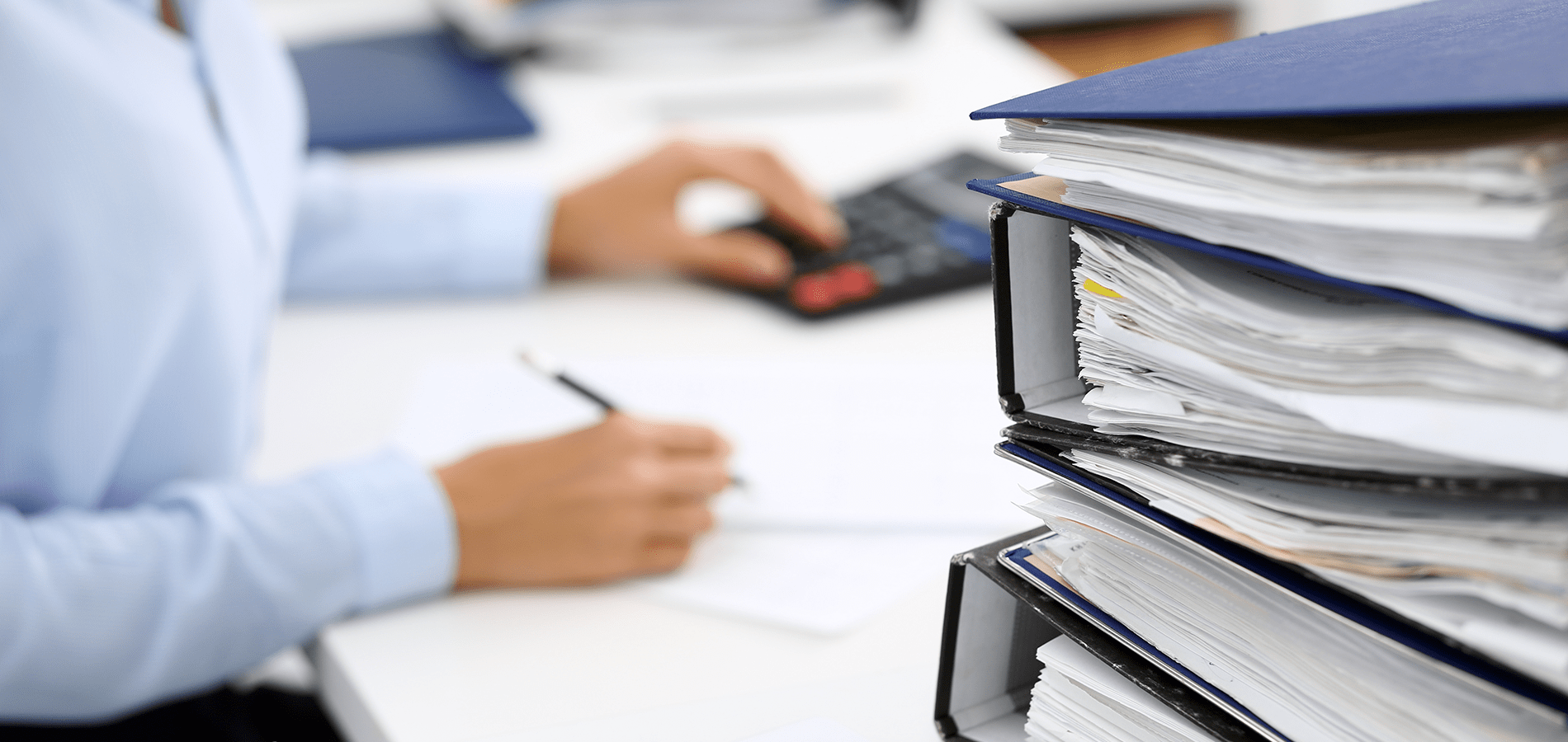 person using calculator with a stack of binders on their desk