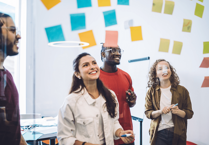 four people looking at a wall filled with post-it notes