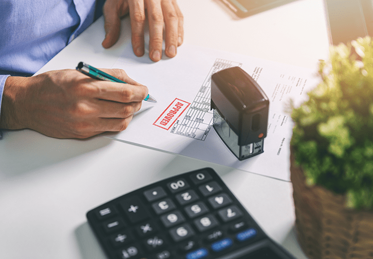 person at desk with stamp and calculator approving a form