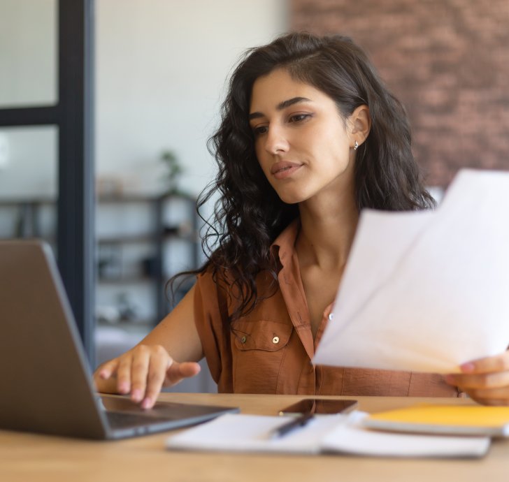 student at laptop holding papers