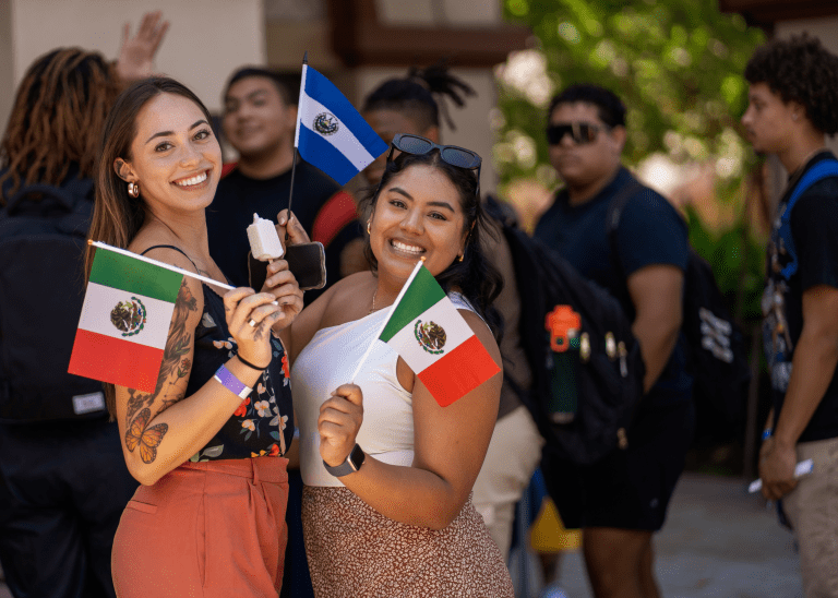 Two smiling women holding small Mexican flags