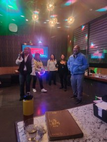 Individuals performing karaoke under colored lights