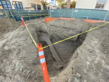 pit dug in ground surrounded by orange construction markers and yellow tape